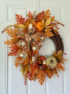 a wreath with pumpkins and leaves hanging on a door