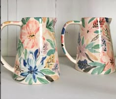 two mugs with floral designs on them are sitting side by side, one is painted pink and the other is blue