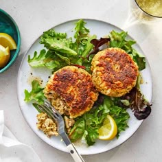 two crab cakes on a plate with salad and lemon wedges