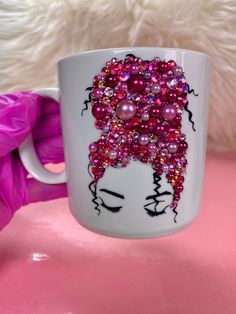 a white coffee mug with pink beads and pearls on the side, sitting on a pink surface