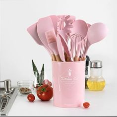 pink utensils are in a cup with tomatoes and other kitchen items around it