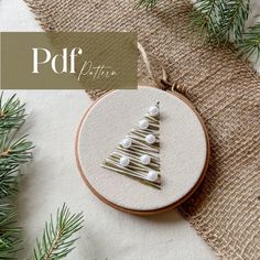 a cross stitch christmas tree ornament on a burlap background with pine needles