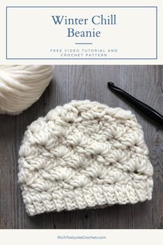 a white crochet beanie sitting on top of a wooden table next to a ball of yarn