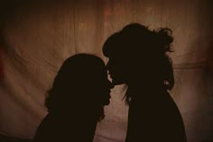 the silhouette of two people are facing each other in front of a white sheeted wall