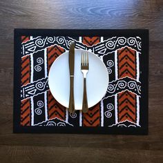 a place mat with an orange and black design on it, next to a fork and knife