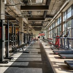 an empty gym with rows of treadmills and windows