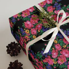 a present wrapped in black and pink floral paper with white ribbon next to pine cones