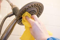 a person cleaning a shower head with a yellow cloth and microfibre duster