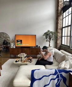 a man sitting on top of a white couch in a living room next to a tv