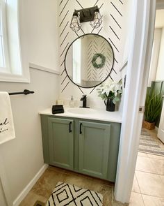 a bathroom with green cabinets and a round mirror on the wall above the sink, along with a black and white rug