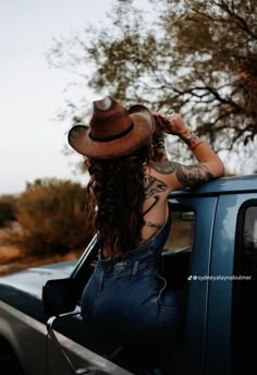 a woman with long hair wearing a hat sitting in the back of a pick up truck