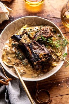 a bowl filled with meat and gravy next to bread on a wooden table