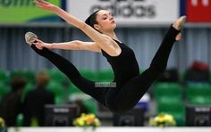 a woman in black is doing a trick on the balance beam with her legs spread out