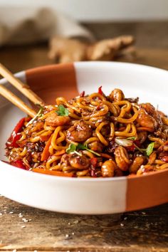 a white bowl filled with noodles and meat on top of a wooden table next to chopsticks