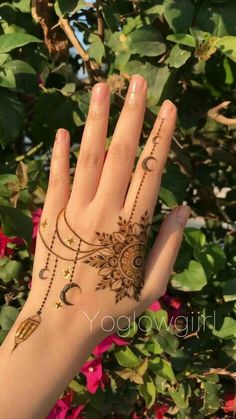 a woman's hand with henna tattoos on it and flowers in the background