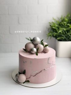 a pink marble cake with silver balls on top and greenery in the back ground