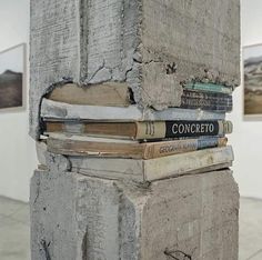 a stack of books sitting on top of a cement pillar next to a brick wall