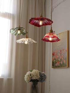 three lights hanging from a ceiling in a room with curtains and flowers on the table