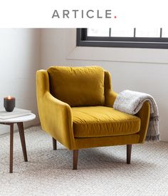 a yellow chair sitting in front of a window next to a table with a candle on it