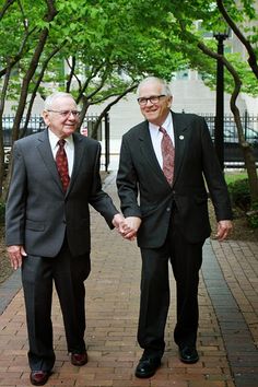 two men in suits are holding hands on a sidewalk