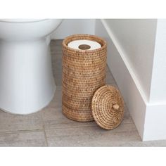 a bathroom with a toilet next to a roll of toilet paper and a basket on the floor