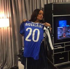 a woman holding up a jersey in front of a tv