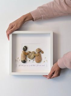 a person holding a framed photo with two small rocks in the shape of people's hands