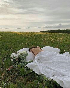 a woman laying on top of a lush green field covered in white cloth next to flowers