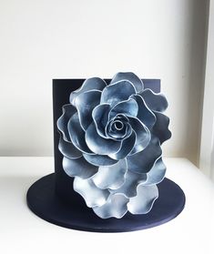 there is a blue and white flower on top of a black hat that looks like it has been made out of paper