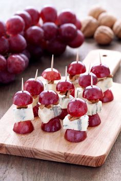 grapes, cheese and nuts are arranged on a wooden cutting board next to some crackers