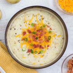 a bowl of potato soup with bacon, cheese and green onions next to other ingredients