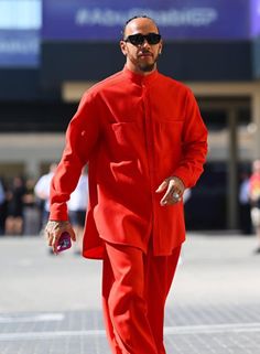 a man in a red suit is walking down the street with sunglasses on his head