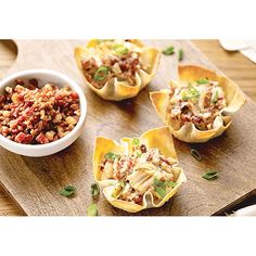 four small cups filled with food sitting on top of a wooden cutting board