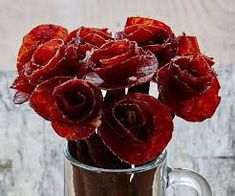 a glass vase filled with red flowers on top of a wooden table next to a wall