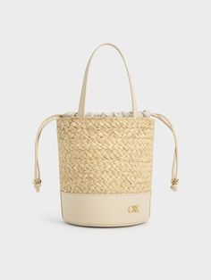 The quintessential bucket bag with a summer-friendly twist. This piece features a classic cylindrical shape, with a leather bottom offering a smooth contrast to the intricate woven finish and providing extra stability. It also includes a drawstring closure for quick and easy access to your belongings while keeping them safe and secure. The emblem adds a subtle touch of glamour in gold, further elevating this sophisticated design. Cheap Summer Cream Bucket Bag, Cheap Gold Bucket Bag, Luxury Leather Basket Bucket Bag, Luxury Straw Bucket Bag With Woven Leather, Luxury Woven Leather Straw Bucket Bag, Chic Leather Bucket Straw Bag, Elegant Leather Bucket Straw Bag, Chic Natural Leather Bucket Bag, Luxury Beige Basket Bucket Bag