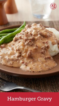 a plate with mashed potatoes and gravy on it next to green beans