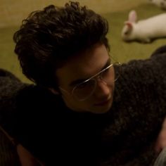 a man laying on the ground next to two white cats and one is wearing glasses