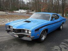 a blue muscle car parked in a parking lot next to snow covered trees and bushes