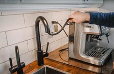 a person is using a coffee maker on a counter top with a sink and faucet