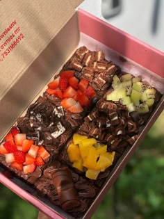 a pink box filled with assorted chocolates and fruit on top of each other