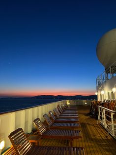 the deck of a cruise ship at night with many empty chairs and lights on it