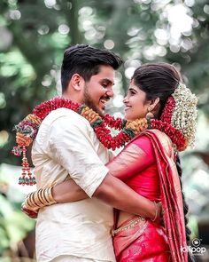 a man and woman standing next to each other in front of trees with garlands around their necks