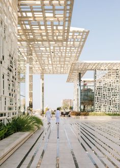 two people walking down a walkway in front of some buildings