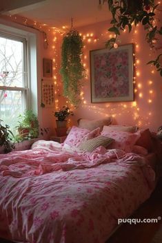 there is a bed with pink comforter and lights on the wall above it, along with potted plants