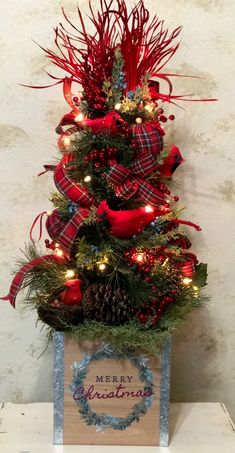 a christmas tree decorated with red ribbon and lights in a wooden box on top of a table