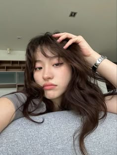 a woman with long brown hair is sitting on a couch and looking at the camera