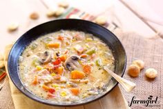 a bowl of soup with mushrooms and carrots on a wooden board next to crackers