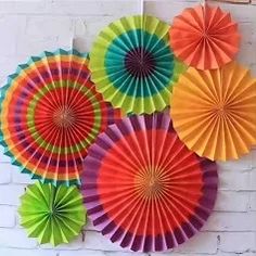 colorful paper fans are hanging on the wall in front of a white brick wall,