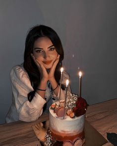 a woman sitting in front of a cake with candles on it and her hand near her face