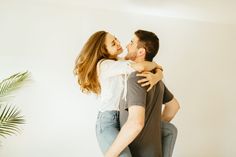 a man and woman hug each other while standing in front of a wall with a potted plant